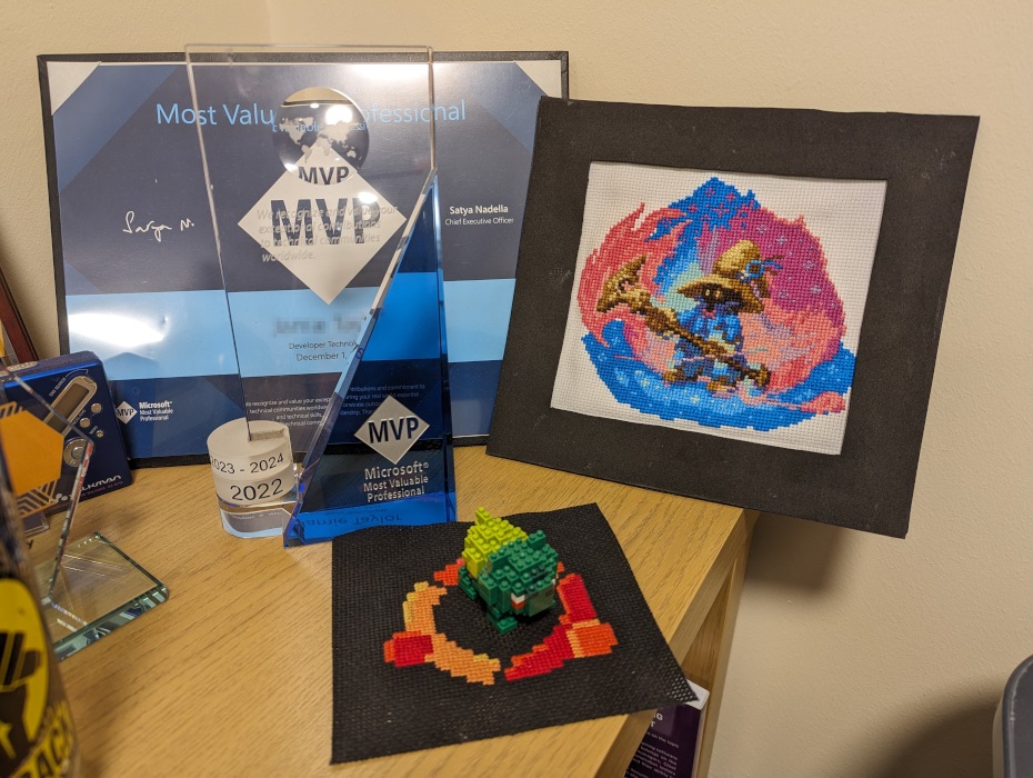 Two cross stitches that Squidge has done for Jay (one of Vivi from Final Fantasy IX and one of the Ubuntu logo) next to some of his awards